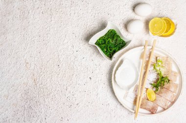 Yemek hazırlama konsepti. Çiğ hake, chukka salatası, limon dilimi, taze otlar, yumurtalar, deniz tuzu. Hafif tonlarda geleneksel Asya yemeği alçı arka plan, üst görünüm