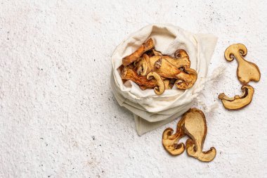 Orman, keten çuvalında kurutulmuş yenilebilir mantar. Susuz dilimler, sağlıklı yemek pişirmek için nefis malzemeler. Açık renk alçı arkaplan, üst görünüm