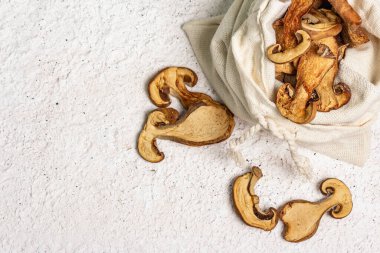 Orman, keten çuvalında kurutulmuş yenilebilir mantar. Susuz dilimler, sağlıklı yemek pişirmek için nefis malzemeler. Açık renk alçı arkaplan, üst görünüm