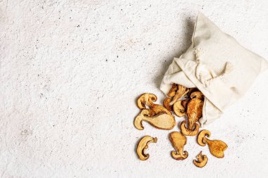 Orman, keten çuvalında kurutulmuş yenilebilir mantar. Susuz dilimler, sağlıklı yemek pişirmek için nefis malzemeler. Açık renk alçı arkaplan, üst görünüm