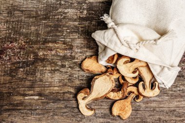 Orman, keten çuvalında kurutulmuş yenilebilir mantar. Susuz dilimler, sağlıklı yemek pişirmek için nefis malzemeler. Kaliteli ahşap masa, üst manzara