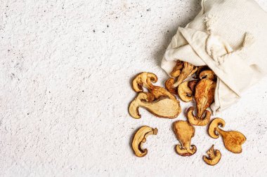 Orman, keten çuvalında kurutulmuş yenilebilir mantar. Susuz dilimler, sağlıklı yemek pişirmek için nefis malzemeler. Açık renk alçı arkaplan, üst görünüm