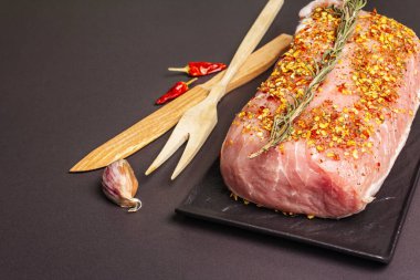 Çiğ domuz filetosu. Biberiye, sarımsak ve baharatlı taze et seramik standı. Ahşap çatal bıçak takımı, siyah taş beton arka plan, kopyalama alanı