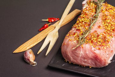 Çiğ domuz filetosu. Biberiye, sarımsak ve baharatlı taze et seramik standı. Ahşap çatal bıçak takımı, siyah taş beton arka plan, kopyalama alanı