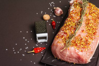 Çiğ domuz filetosu. Biberiye, sarımsak ve baharatlı taze et seramik standı. Öğütücü, kurutulmuş biber, tuz, siyah taş beton arka plan, üst manzara.