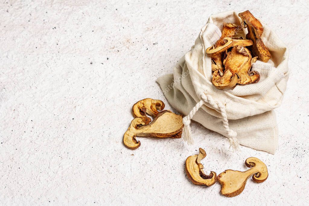 Forest dried edible mushrooms in a linen sack. Dehydrated slices, exquisite ingredient for cooking healthy food. Light colors plaster background, copy space