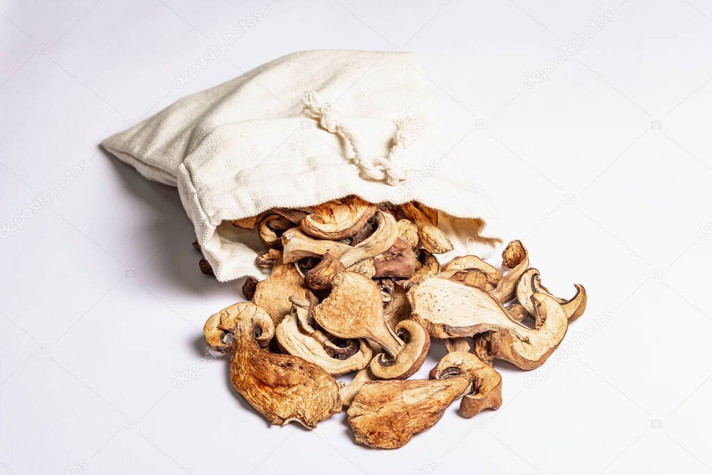 Forest dried edible mushrooms in a linen sack isolated on white background. Dehydrated slices, exquisite ingredient for cooking healthy food