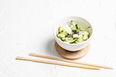 Beyaz seramik kasede susam tohumlu taze salatalık. Vitamin bahar yiyeceği, sağlıklı beslenme konsepti. Beyaz alçı arkaplan, metin için yer