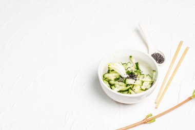 Beyaz seramik kasede susam tohumlu taze salatalık. Vitamin bahar yiyeceği, sağlıklı beslenme konsepti. Beyaz alçı arkaplan, metin için yer