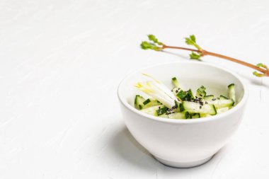 Beyaz seramik kasede susam tohumlu taze salatalık. Vitamin bahar yiyeceği, sağlıklı beslenme konsepti. Beyaz alçı arkaplan, metin için yer