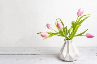 Beyaz arka planda seramik vazoda yumuşak pembe laleler. Bayram hediyesi, Paskalya, doğum günü, sevgililer günü veya düğün için tebrik kartı. Tatil konsepti, metin için bir yer