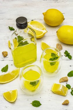 Geleneksel İtalyan sindirimi: limonlu limonata ve kokulu nane yapraklı limoncello. Alkolsüz içecek beyaz tahta arka planda, yakın plan.
