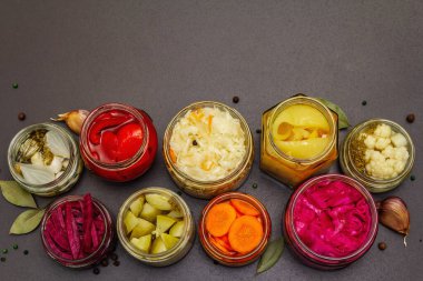 Cam kavanozlarda mayalanmış sebzeler. Mevsimlik sebze konsepti, sağlıklı yaşam tarzı için probiyotik gıdası. Siyah taş arkaplan, üst görünüm