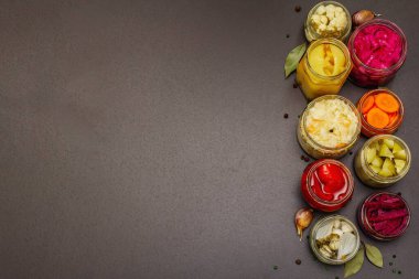 Cam kavanozlarda mayalanmış sebzeler. Mevsimlik sebze konsepti, sağlıklı yaşam tarzı için probiyotik gıdası. Siyah taş arkaplan, üst görünüm