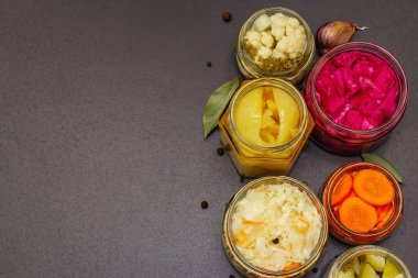 Cam kavanozlarda mayalanmış sebzeler. Mevsimlik sebze konsepti, sağlıklı yaşam tarzı için probiyotik gıdası. Siyah taş arkaplan, üst görünüm