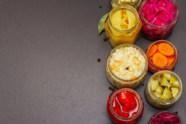 Assorted of fermented vegetables in glass jars. Preserved season vegetables concept, probiotics food for healthy lifestyle. Black stone concrete background, top view