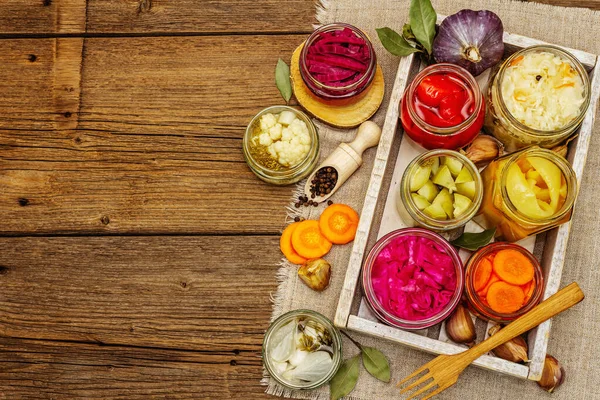 Assorted of fermented vegetables in glass jars. Preserved season vegetables concept, probiotics food for healthy lifestyle. Vintage wooden table, top view