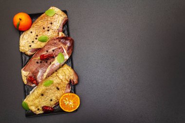 Çiğ ördek göğsü, deniz tuzu, taze fesleğen, mandalina ve baharat. Kümes hayvanları, doğal BIO ürünü, evcil kümes hayvanı. Siyah taş arkaplan, üst görünüm