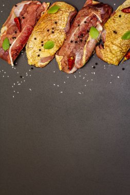 Çiğ ördek göğsü, deniz tuzu, taze fesleğen, acı biber ve baharat. Kümes hayvanları, doğal BIO ürünü, evcil kümes hayvanı. Siyah taş arkaplan, üst görünüm