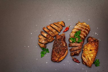 Taze maydanozlu, acılı ve karabiberli kızarmış ördek göğsü, deniz tuzu. Lezzetli yemekler, siyah taştan kesilmiş etler betondan arka plan, üst manzara.