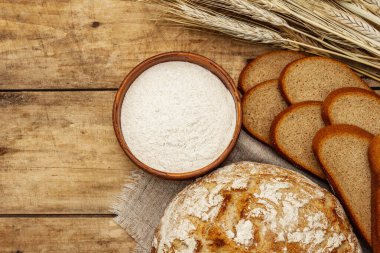 Buğday kulaklı taze ekmek ve bir kase un. Kaliteli ahşap masa, hamur yoğurma, üst manzara.