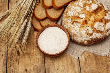 Buğday kulaklı taze ekmek ve bir kase un. Kaliteli ahşap masa, hamur yoğurma, üst manzara.