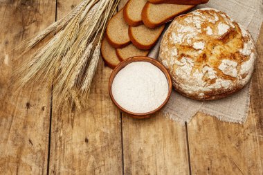 Buğday kulaklı taze ekmek ve bir kase un. Kaliteli ahşap masa, hamur yoğurma, üst manzara.
