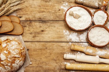 Buğday kulaklı taze ekmek ve bir kase un ve tahıl, yuvarlanan raptiyeler. Kaliteli ahşap masa, hamur yoğurma, üst manzara.
