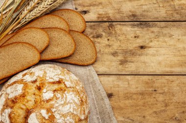 Buğday kulaklı ve dilimli taze ekmek. Kaliteli ahşap masa, hamur yoğurma, üst manzara.