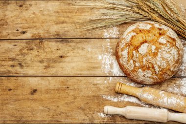 Buğday kulaklı ve okkalı taze ekmek. Kaliteli ahşap masa, hamur yoğurma, üst manzara.