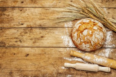 Buğday kulaklı ve okkalı taze ekmek. Kaliteli ahşap masa, hamur yoğurma, üst manzara.