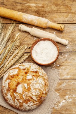 Buğday kulaklı taze ekmek, bir kase un ve oklavalarla. Kaliteli ahşap masa, hamur yoğurma, üst manzara.