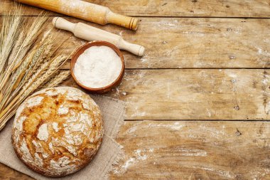 Buğday kulaklı taze ekmek, bir kase un ve oklavalarla. Kaliteli ahşap masa, hamur yoğurma, üst manzara.