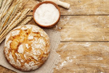 Buğday kulaklı taze ekmek, bir kase un ve oklavalarla. Kaliteli ahşap masa, hamur yoğurma, üst manzara.