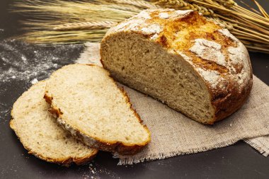 Tahta tezgahta buğday kulaklı taze ekmek. Dilimler ve keten peçete. Siyah taş beton arka plan, kapat