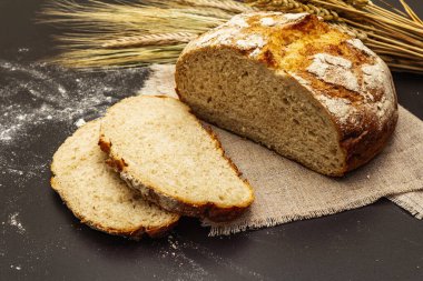 Tahta tezgahta buğday kulaklı taze ekmek. Dilimler ve keten peçete. Siyah taş beton arka plan, kapat