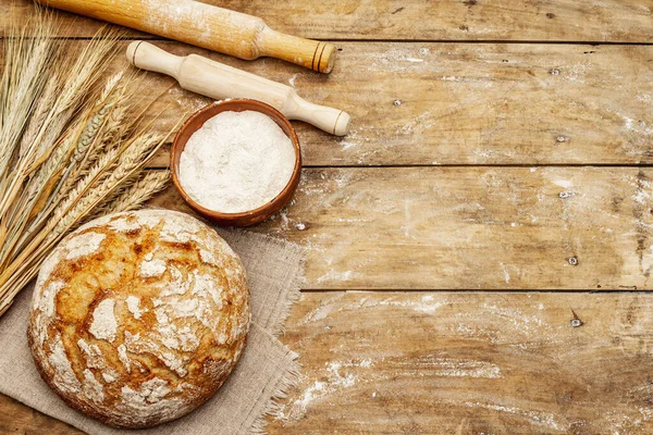 Buğday kulaklı taze ekmek, bir kase un ve oklavalarla. Kaliteli ahşap masa, hamur yoğurma, üst manzara.