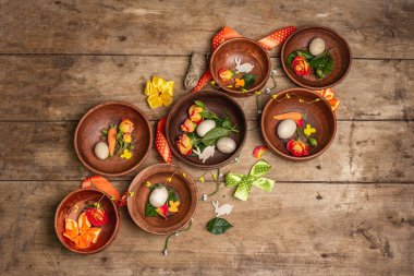 Paskalya seramik kaseleri, yumurtalar, tavşanlar ve eski bir masada taze güller. Geleneksel yemek koleksiyonu, taze çiçekler ve şenlikli dekorasyon. Tahta kaplama arka plan, üst görünüm