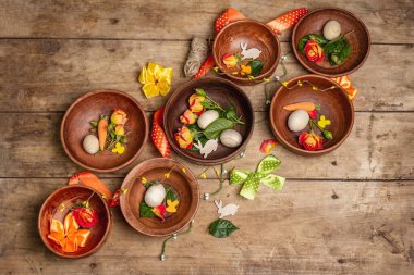 Paskalya seramik kaseleri, yumurtalar, tavşanlar ve eski bir masada taze güller. Geleneksel yemek koleksiyonu, taze çiçekler ve şenlikli dekorasyon. Tahta kaplama arka plan, üst görünüm