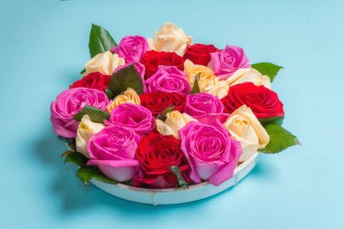 Seramik standında çok renkli taze güllerin kompozisyonu. Düğünler, doğum günleri, 8 Mart, anneler günü ya da sevgililer günü için festival konsepti. Tebrik kartı, düz yatış, mat mavi arkaplan