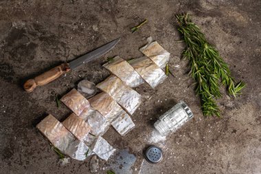 Raw frozen hake pieces with ice, sea salt, vintage knife and fresh rosemary. Healthy food concept, the cooking fish process. Dark marble stone background, top view