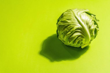 Taze taze lahana, parlak yeşil arka planda koca bir kafa. Modern sert ışık, karanlık gölge. Bahar salatası kesmek için sebzeler. Vejetaryen yemeği, diyet, vitamin