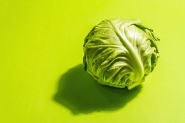 Taze taze lahana, parlak yeşil arka planda koca bir kafa. Modern sert ışık, karanlık gölge. Bahar salatası kesmek için sebzeler. Vejetaryen yemeği, diyet, vitamin