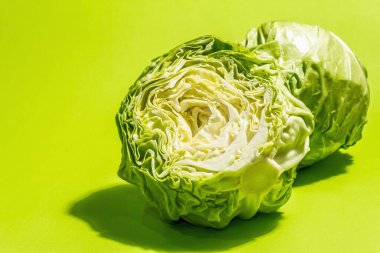 Taze taze lahana, parlak yeşil arka planda yarısı ve tamamı. Modern sert ışık, karanlık gölge. Bahar salatası kesmek için sebzeler. Vejetaryen yemeği, diyet, vitamin