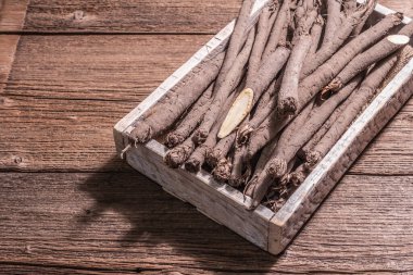 Çiğ Scorzonera ya da İspanyol tuzunu bir sandıkta. Modern sebzeler, sağlıklı yiyecekler, şeker hastaları için uygun. Modaya uygun sert bir ışık, karanlık gölge, ahşap masa, kopyalama alanı