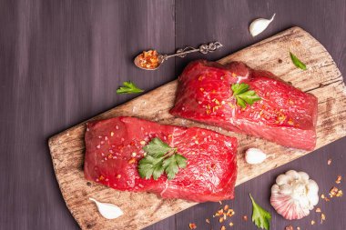 Tahta kesme tahtasında çiğ biftek. Baharatlar, taze sarımsak ve maydanoz. Siyah tahta tahta arka plan, üst görünüm