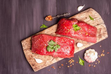 Tahta kesme tahtasında çiğ biftek. Baharatlar, taze sarımsak ve maydanoz. Siyah tahta tahta arka plan, üst görünüm