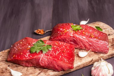 Tahta kesme tahtasında çiğ biftek. Baharatlar, taze sarımsak ve maydanoz. Siyah tahta kaplama arka plan, kapat
