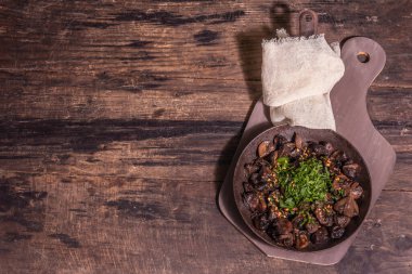 Eski bir dökme demir tavada kızarmış kraliyet şampiyonları. Modaya uygun sert ışık, karanlık gölge. Antika ahşap masa, kırsal gıda tarzı konsept, üst görünüm