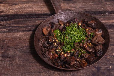 Eski bir dökme demir tavada kızarmış kraliyet şampiyonları. Modaya uygun sert ışık, karanlık gölge. Antika ahşap masa, kırsal gıda tarzı konsept, kopyalama alanı